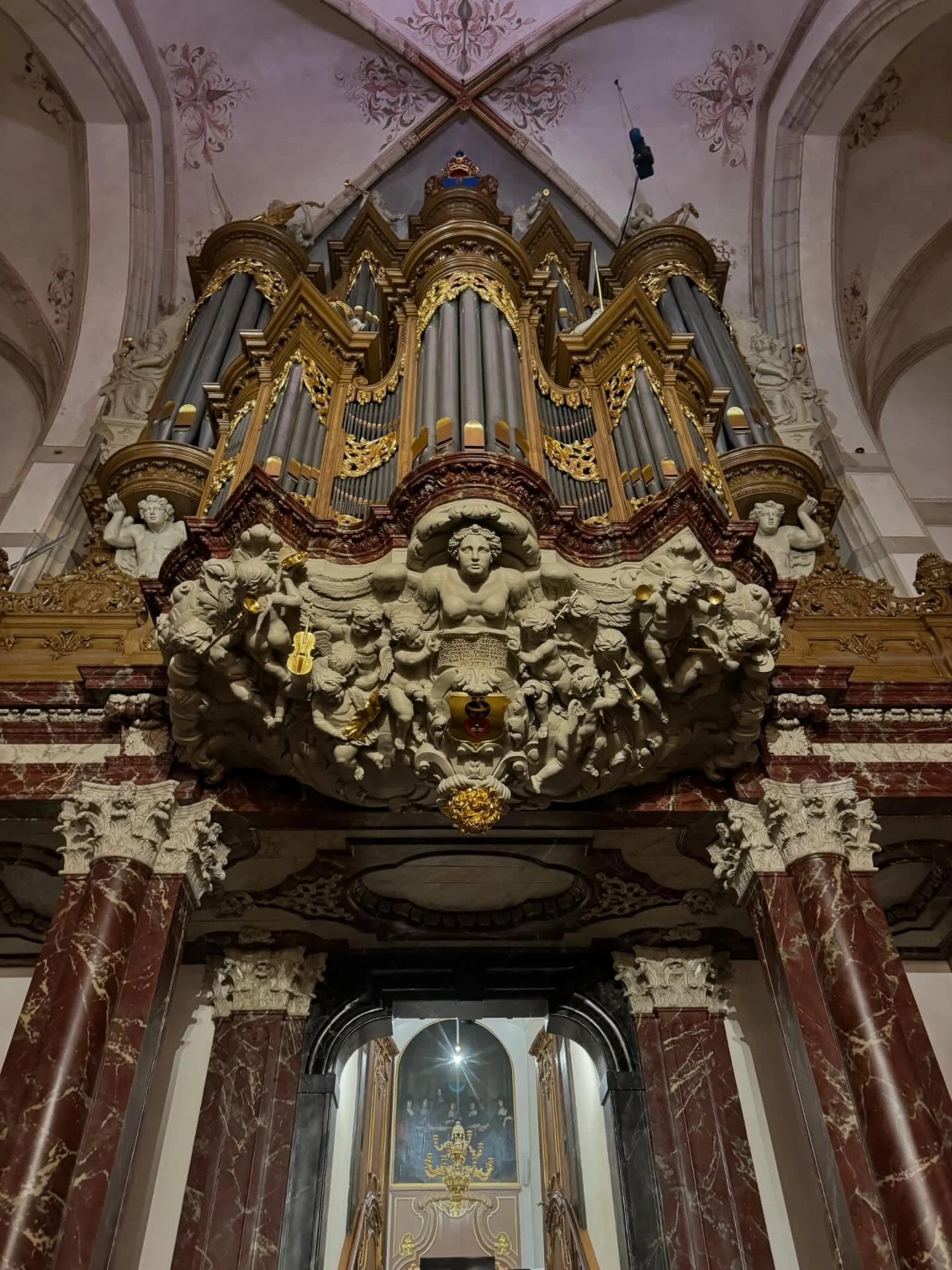 An elaborate church organ with gold trim, carved figures and red marble columns.
