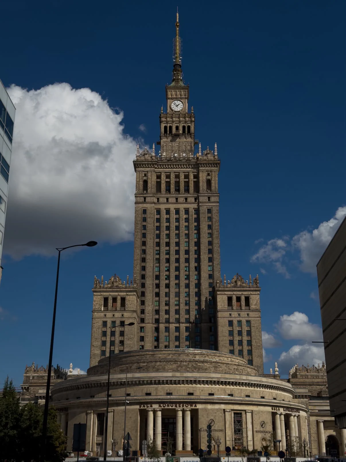 The stone clock tower of Warsaw’s Palace of Culture and Science beneath white clouds and deep blue sky.
