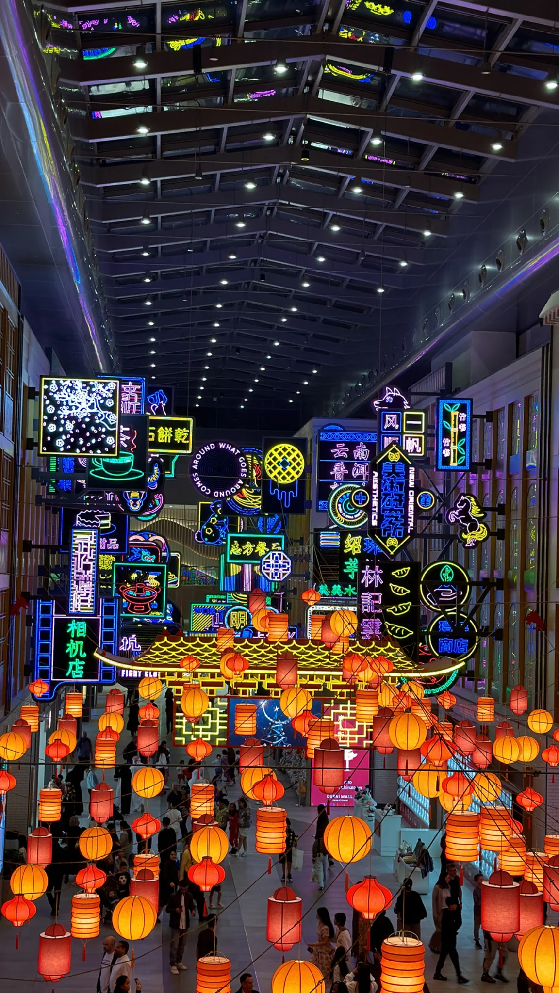 Rows of glowing orange lanterns and colourful illuminated signs beneath a high dark roof.