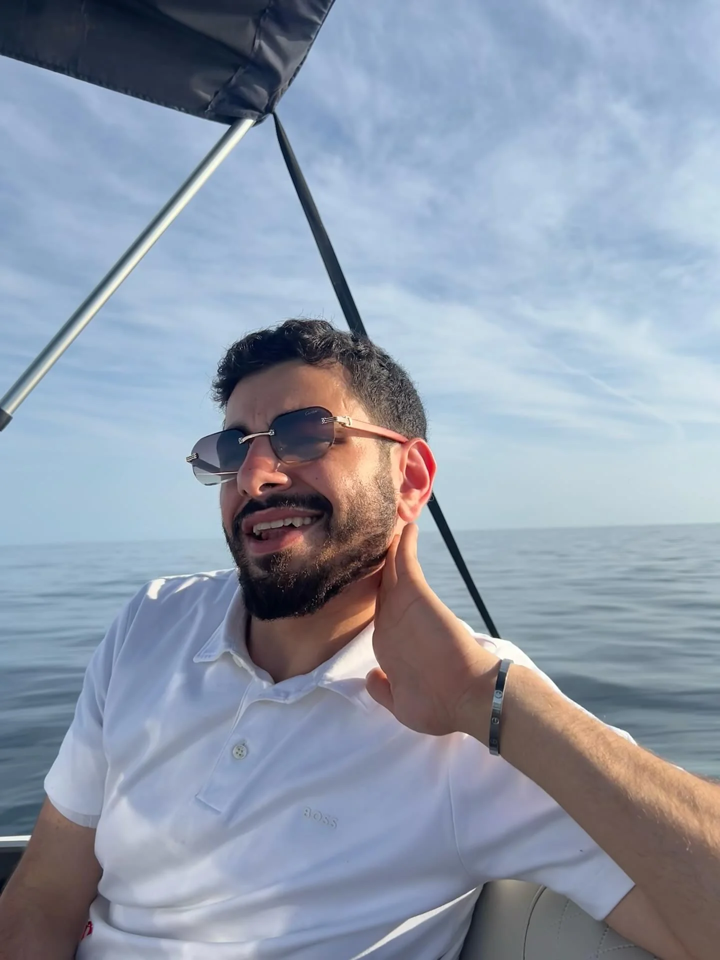 A smiling portrait in a white polo and sunglasses on a boat, with the open sea behind.