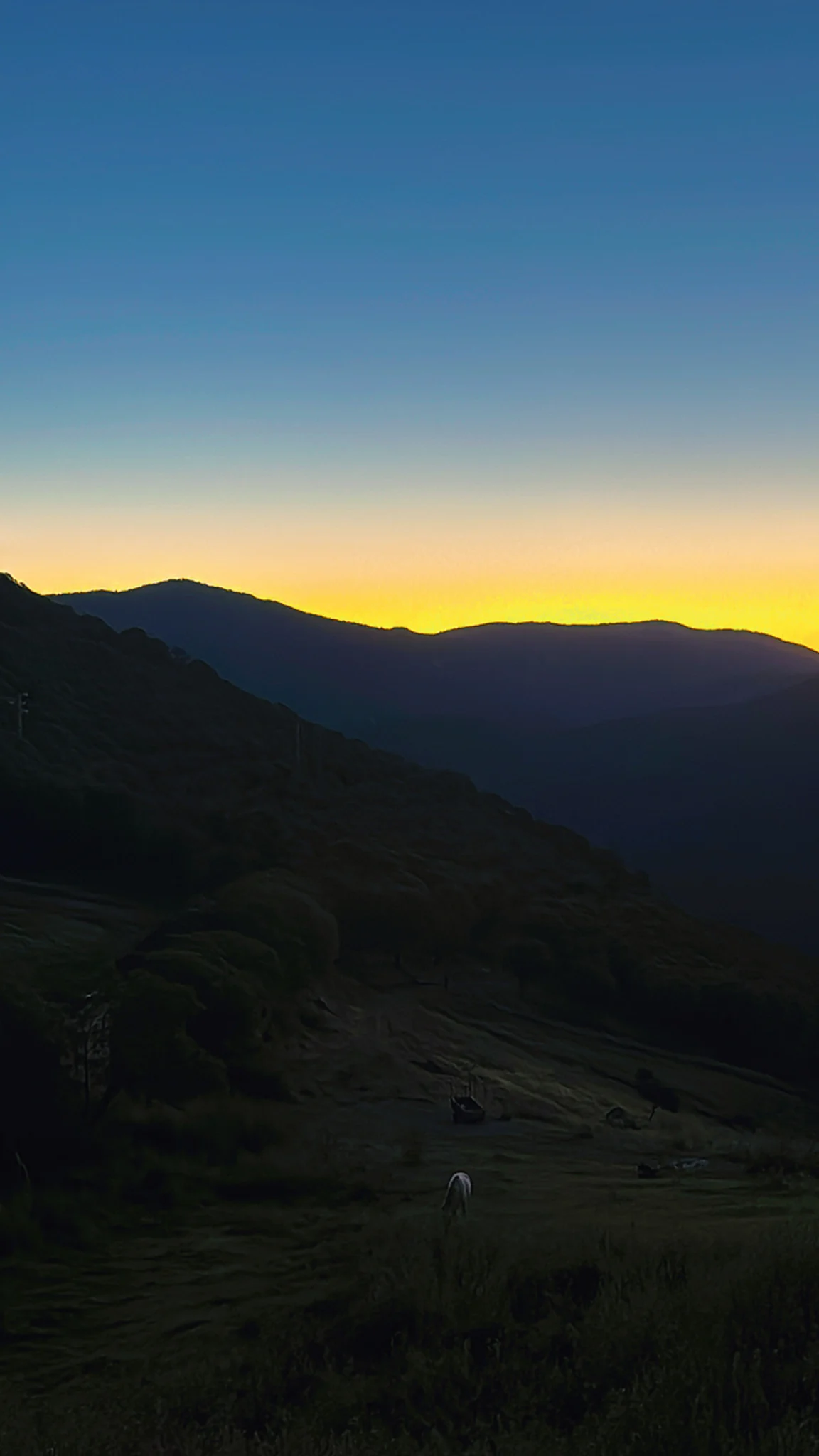 A yellow band of sunset behind dark mountain ridges somewhere in Spain, beneath a blue evening sky.
