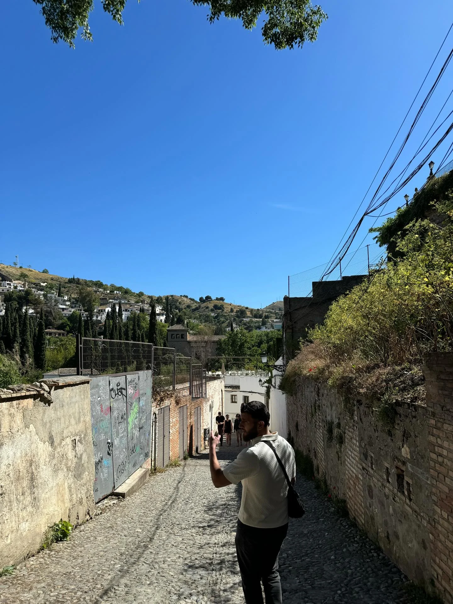 Walking down a sunlit cobbled lane between old walls in Spain.